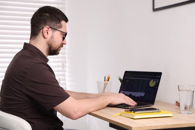 Photo of Stock exchange. Man analysing financial market on laptop at desk indoors