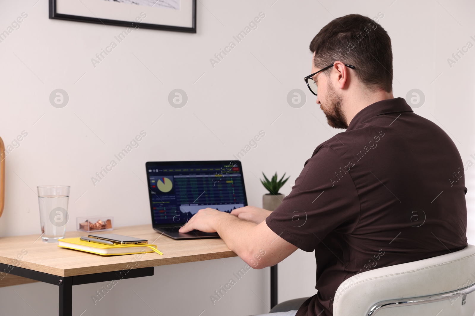 Photo of Stock exchange. Man analysing financial market on laptop at desk indoors