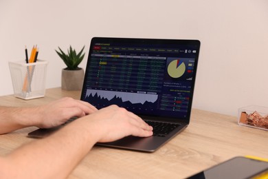 Photo of Stock exchange. Man analysing financial market on laptop at desk indoors, closeup