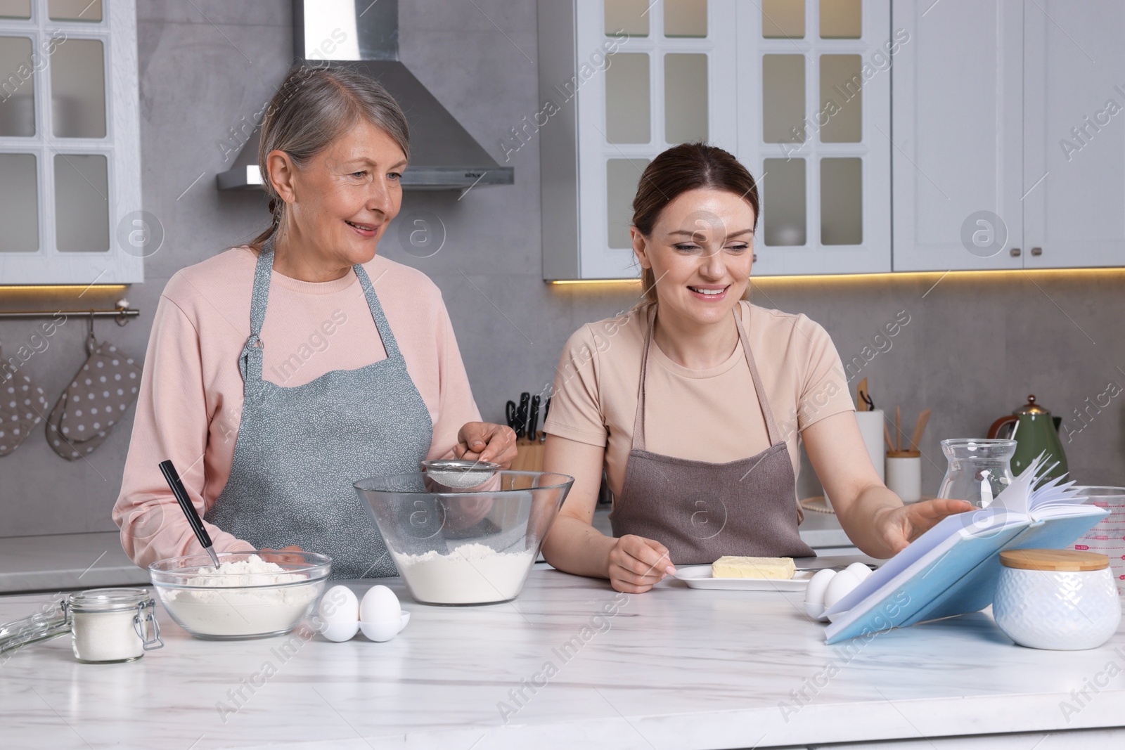 Photo of Happy women cooking by recipe book in kitchen