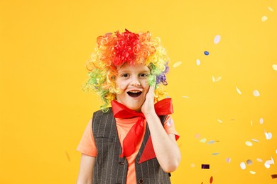 Photo of Happy little boy dressed like clown and flying confetti on orange background. Surprise party