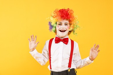 Photo of Happy little boy dressed like clown on yellow background. Surprise party