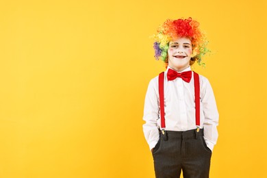 Photo of Happy little boy dressed like clown on yellow background, space for text. Surprise party