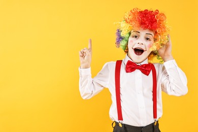 Photo of Emotional little boy dressed like clown pointing upwards on yellow background, space for text. Surprise party