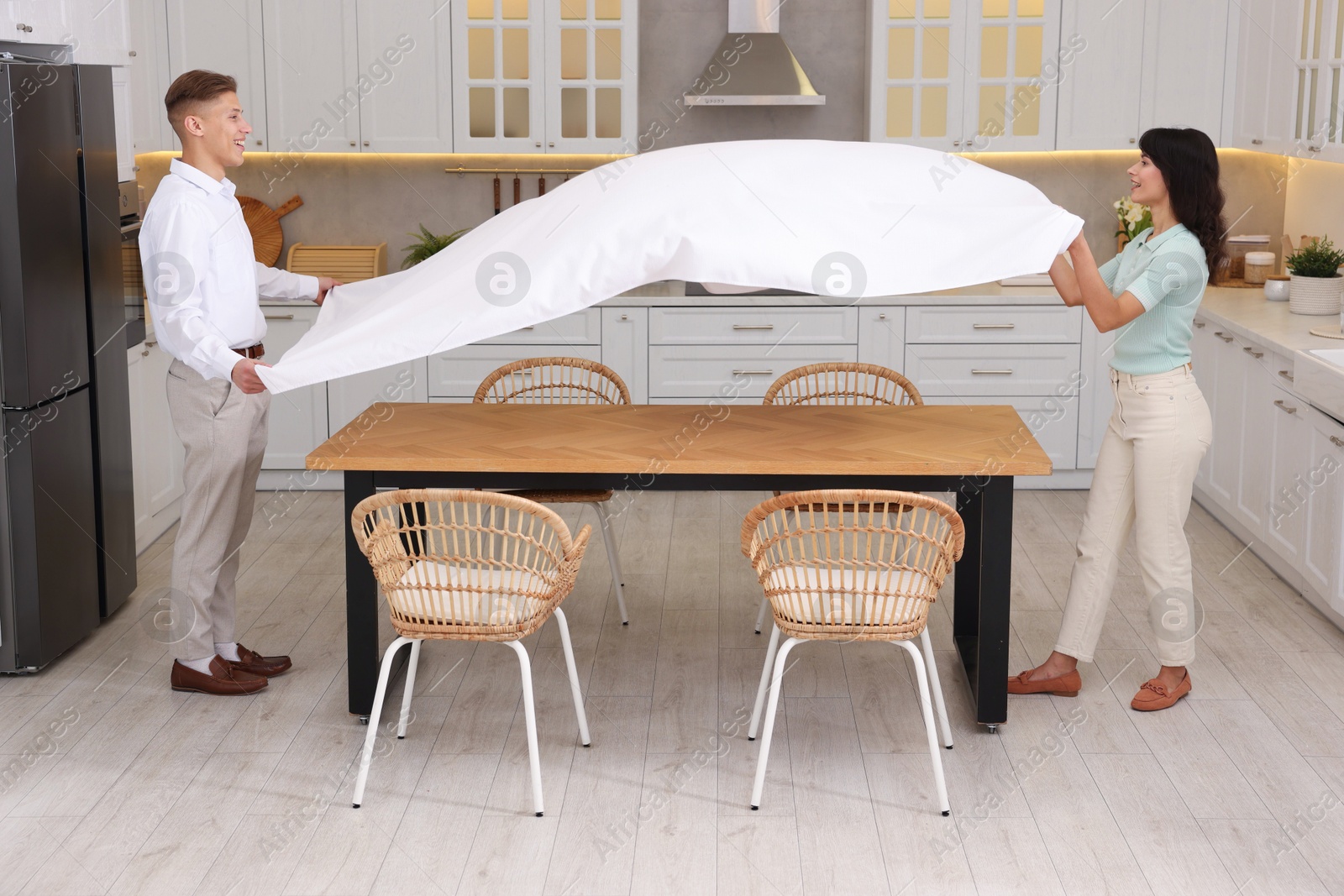 Photo of Couple putting white tablecloth on table in kitchen