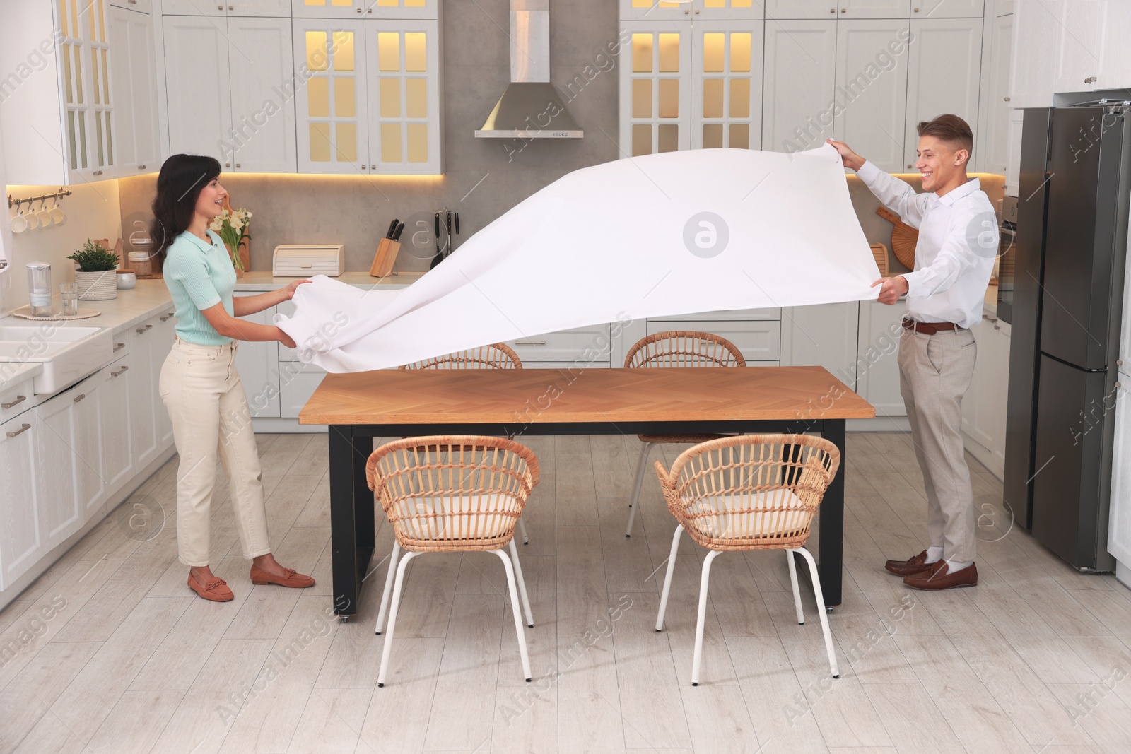 Photo of Couple putting white tablecloth on table in kitchen