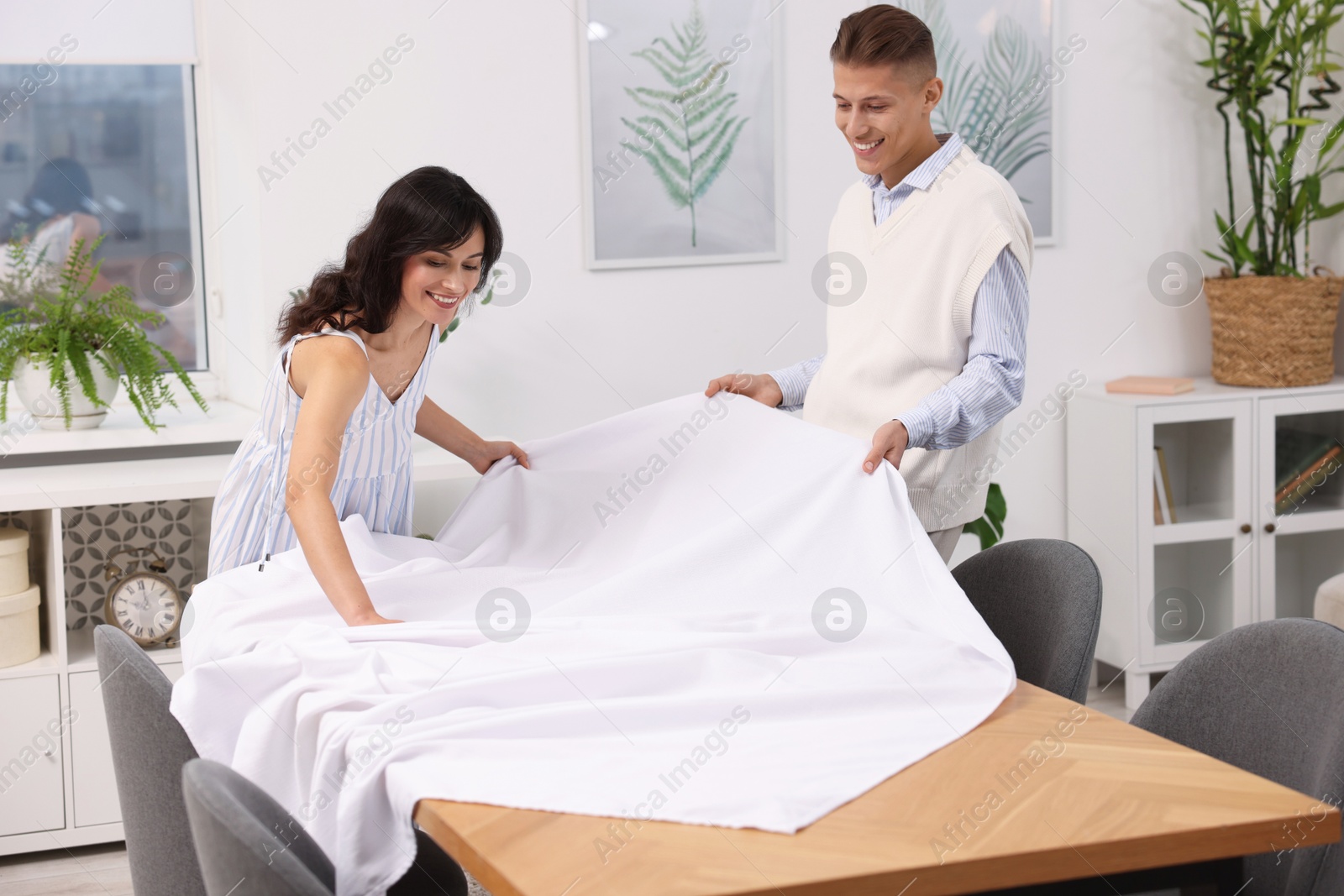 Photo of Couple putting white tablecloth on table at home