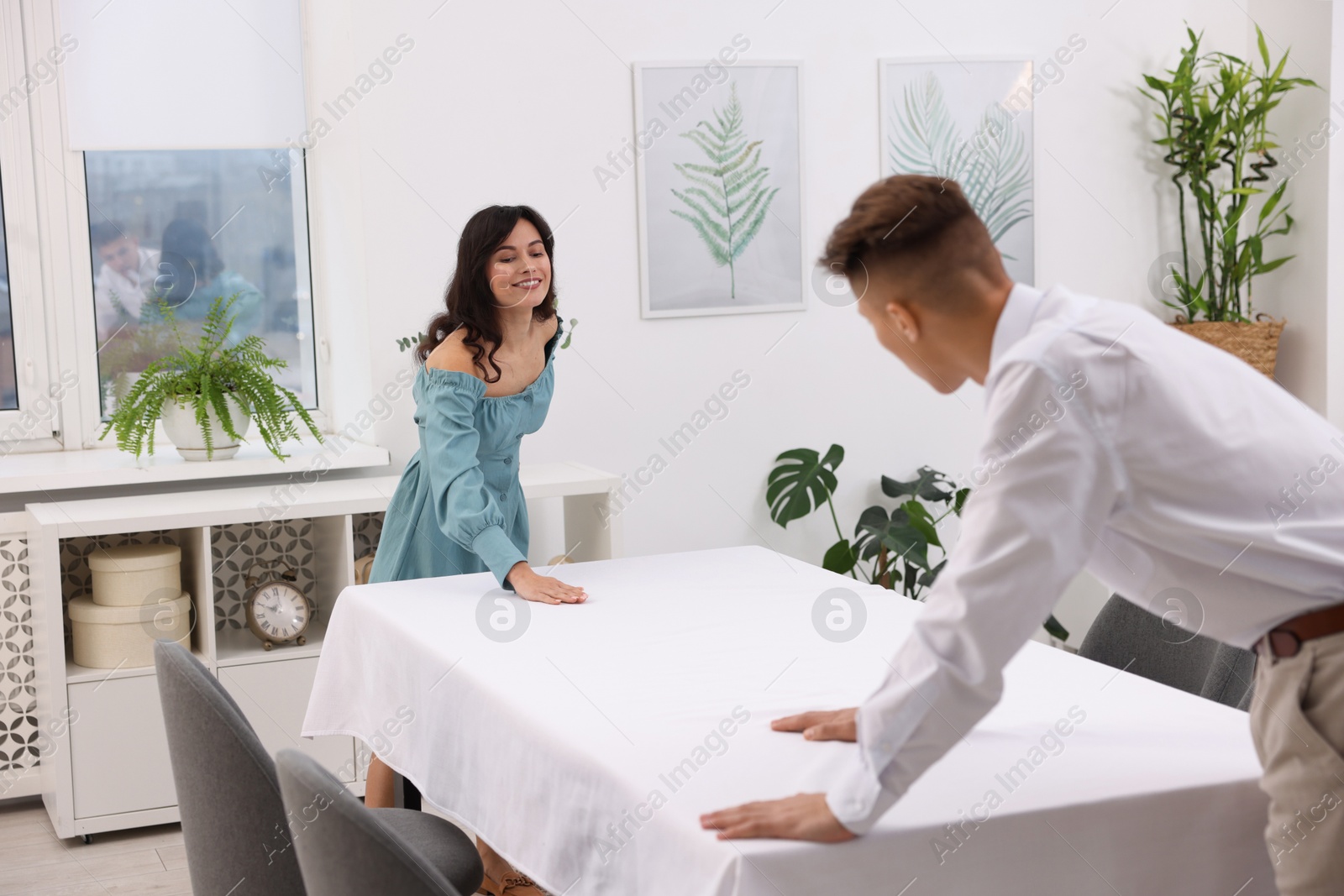 Photo of Couple putting white tablecloth on table at home