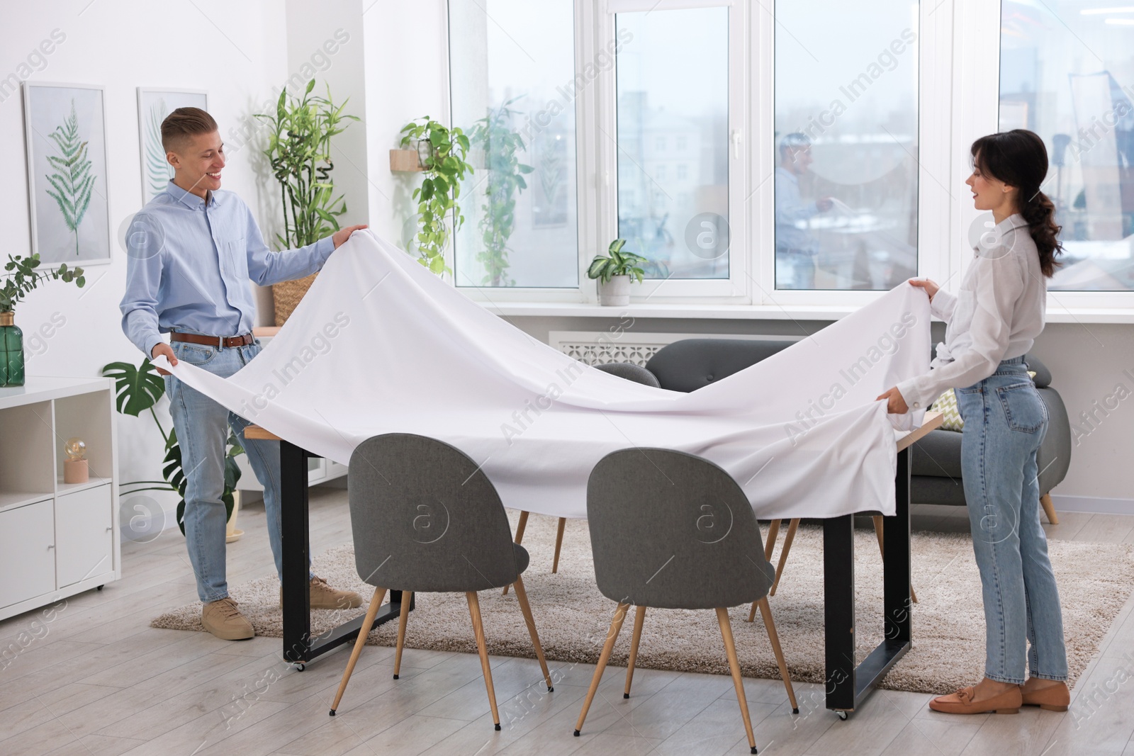 Photo of Couple putting white tablecloth on table at home