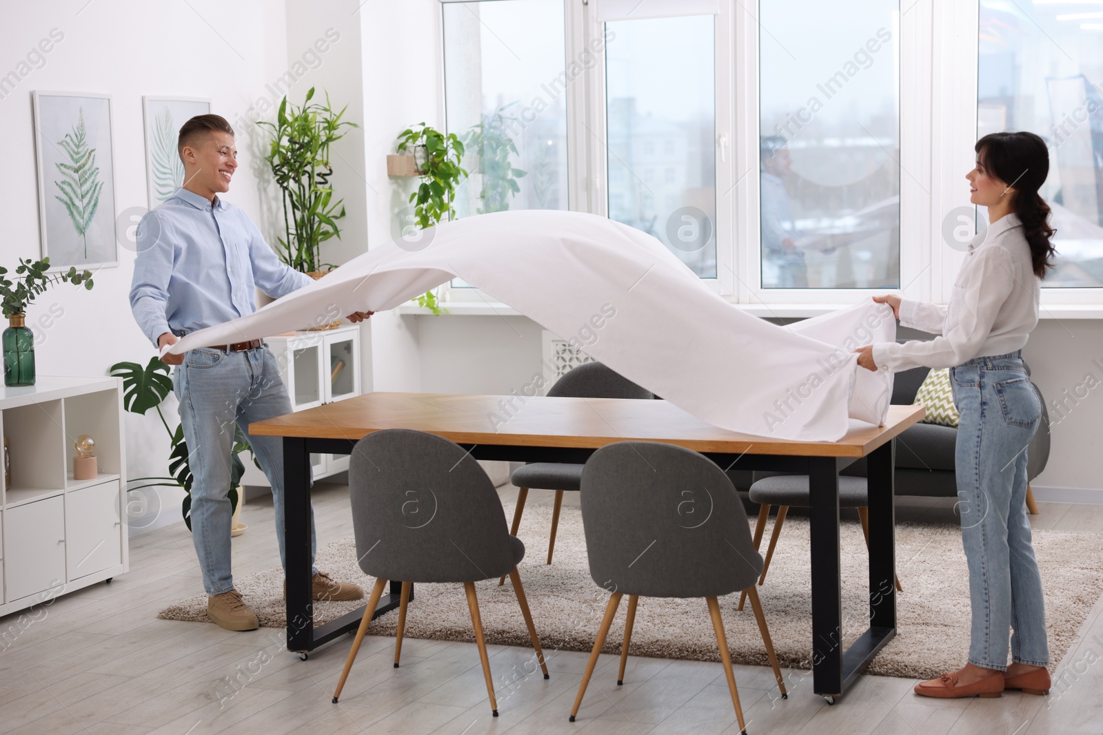 Photo of Couple putting white tablecloth on table at home