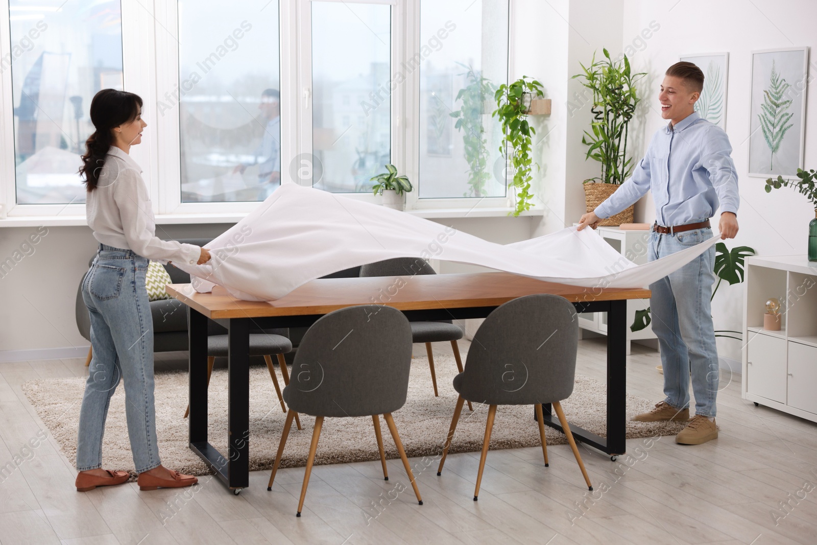 Photo of Couple putting white tablecloth on table at home