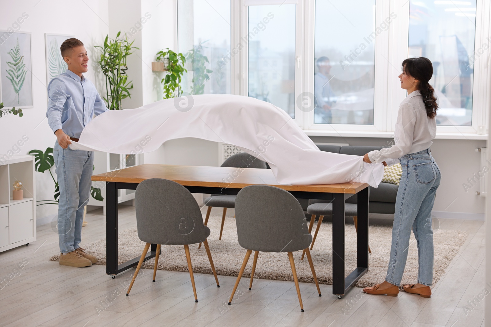 Photo of Couple putting white tablecloth on table at home