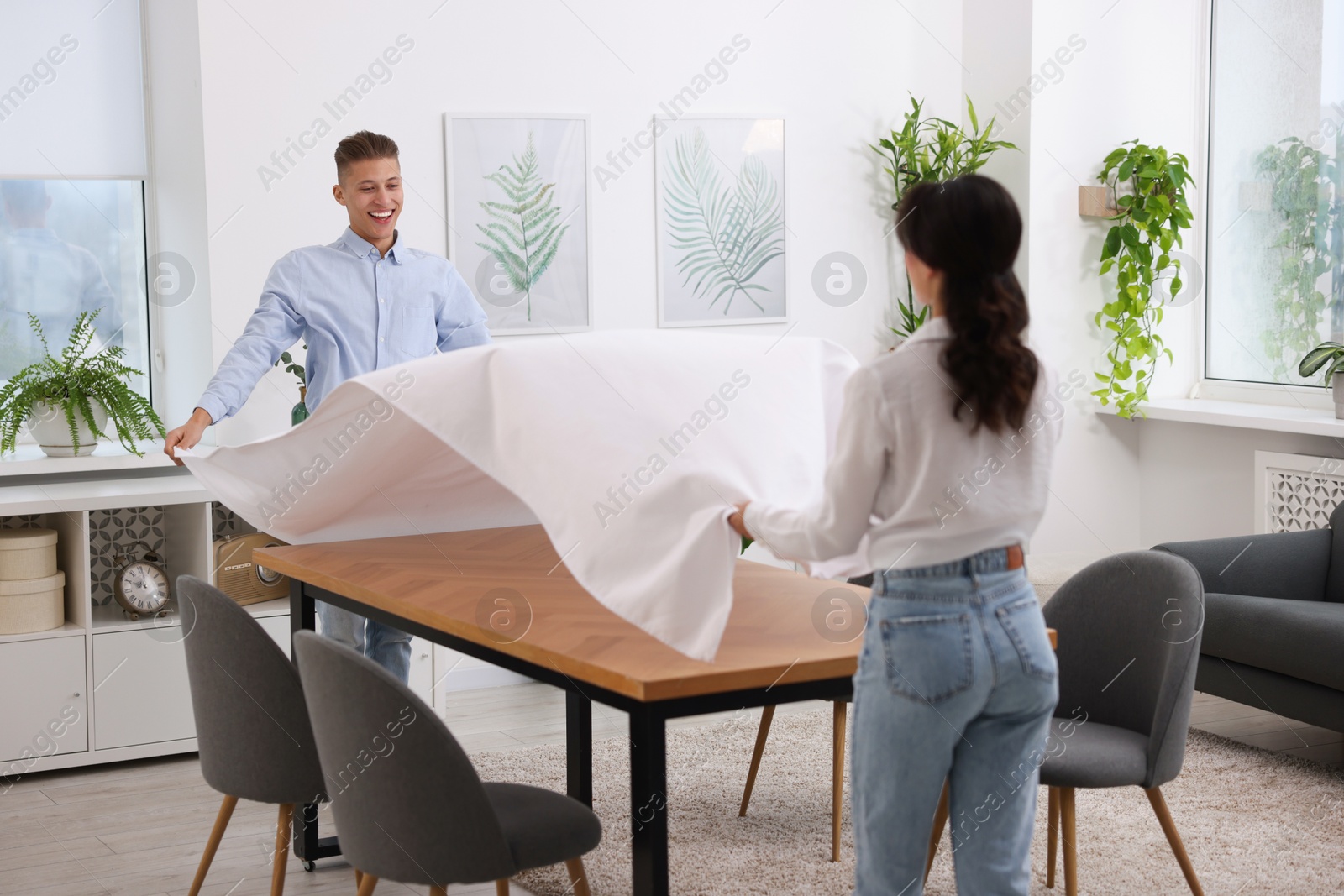 Photo of Couple putting white tablecloth on table at home