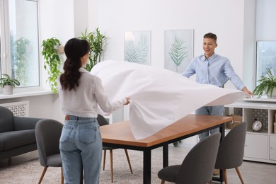 Couple putting white tablecloth on table at home