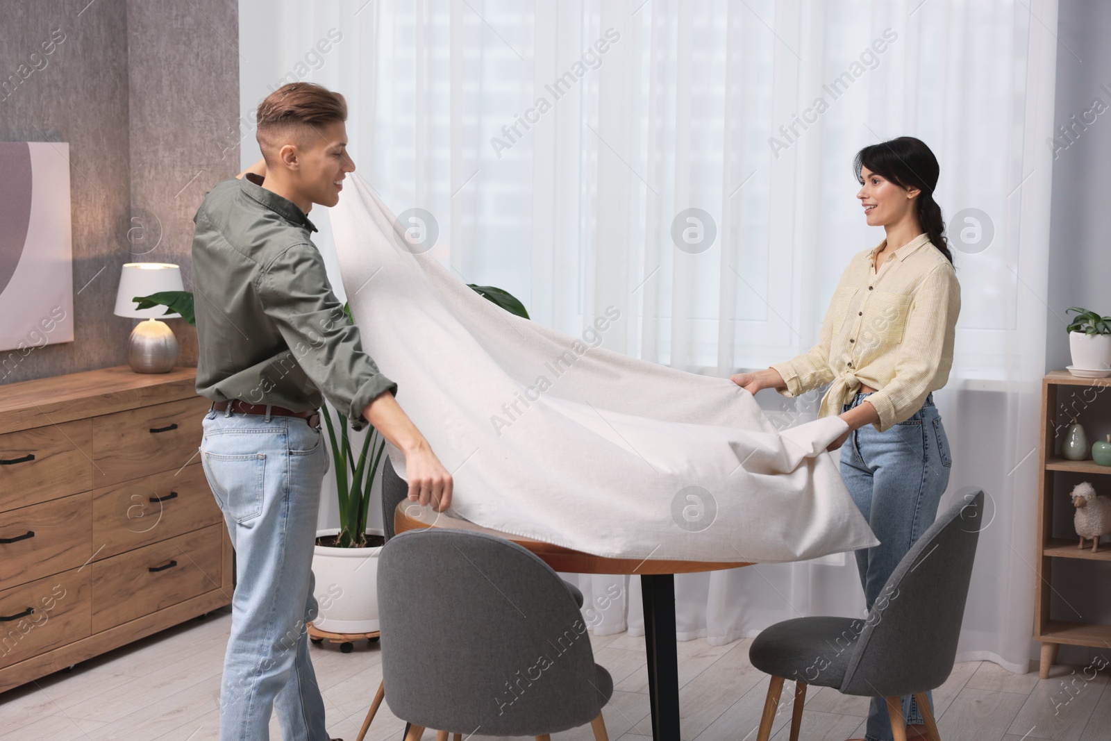 Photo of Couple putting white tablecloth on table at home