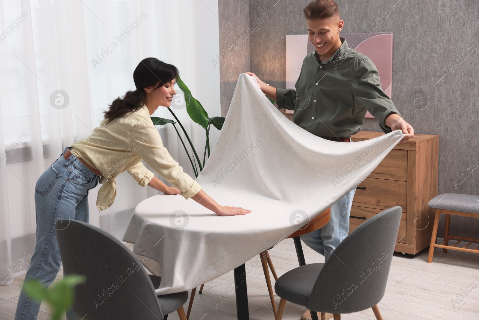 Photo of Couple putting white tablecloth on table at home