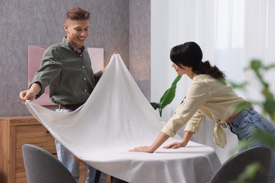 Photo of Couple putting white tablecloth on table at home