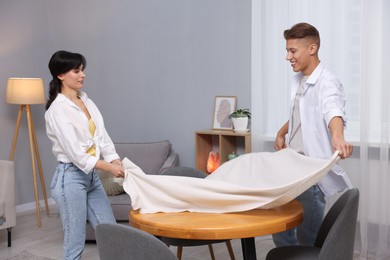 Photo of Couple putting white tablecloth on table at home