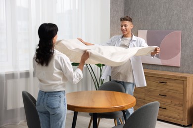 Couple putting white tablecloth on table at home