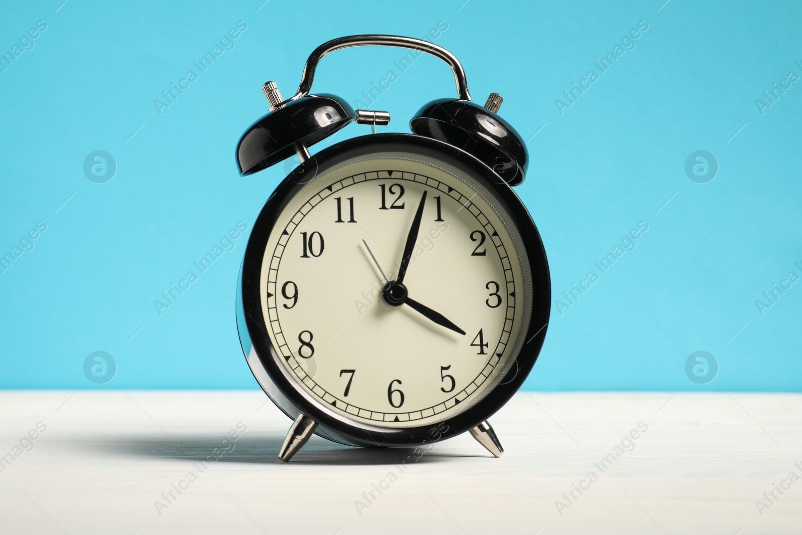 One black clock on white wooden table against light blue background Photo of One black clock on white wooden table against light blue background