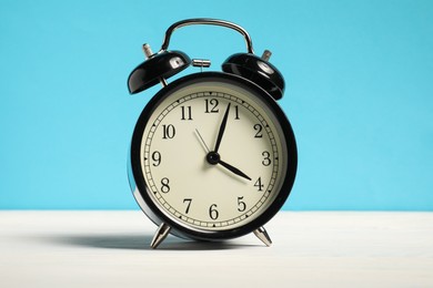 Photo of One black clock on white wooden table against light blue background
