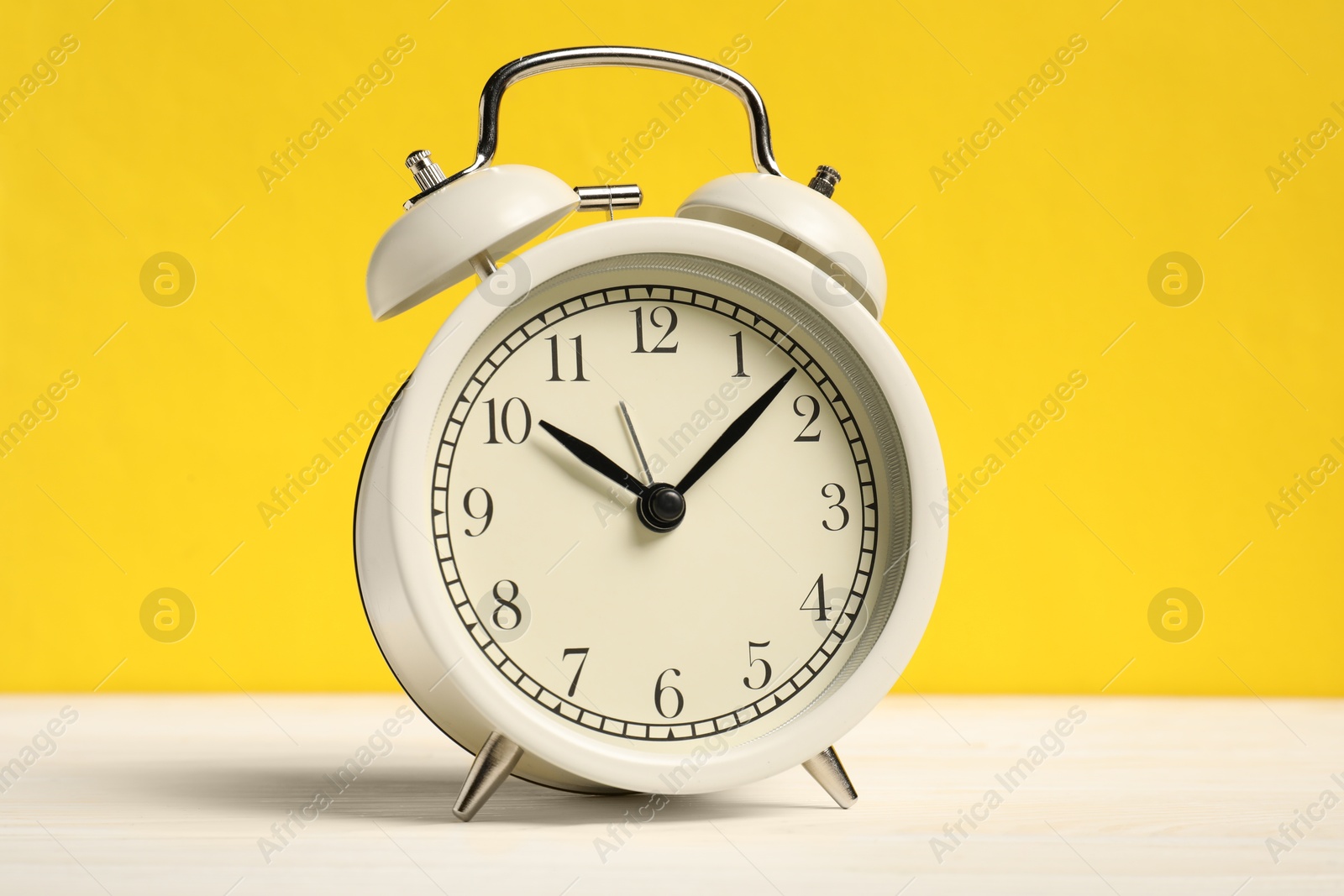 One alarm clock on white wooden table against yellow background Photo of One alarm clock on white wooden table against yellow background