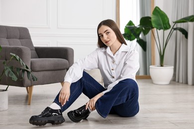 Photo of Beautiful young woman in stylish jeans sitting on floor at home