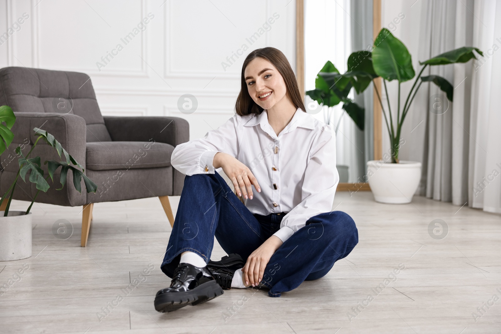 Photo of Smiling woman in stylish jeans sitting on floor at home