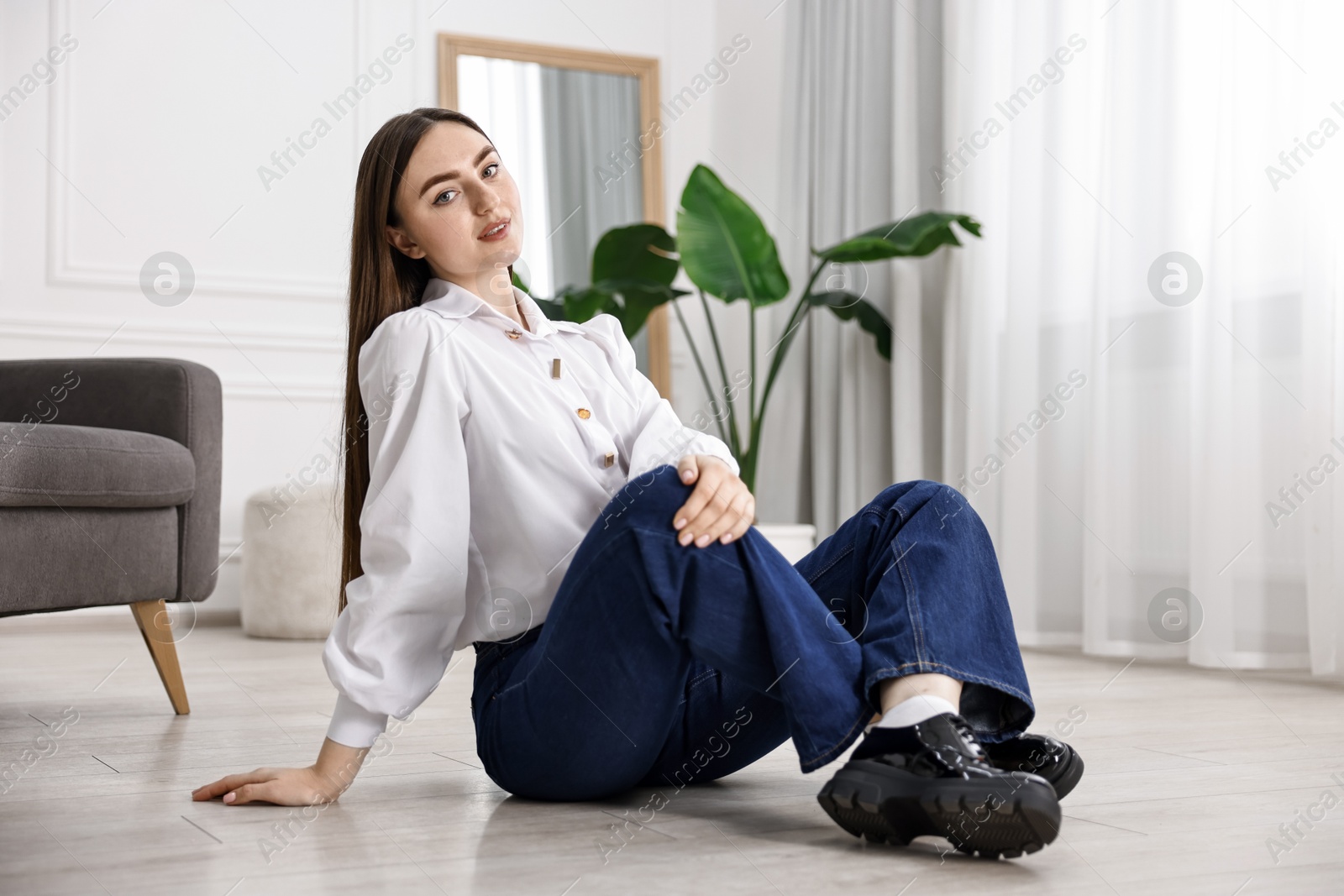 Photo of Beautiful young woman in stylish jeans sitting on floor at home