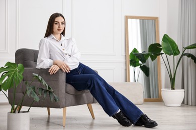 Photo of Woman in stylish jeans on armchair at home