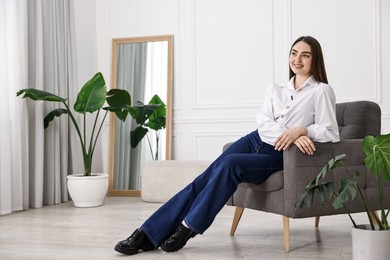 Smiling woman in stylish jeans on armchair at home