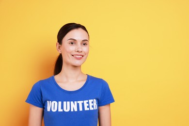 Photo of Young beautiful volunteer wearing t-shirt with printed word on orange background. Space for text