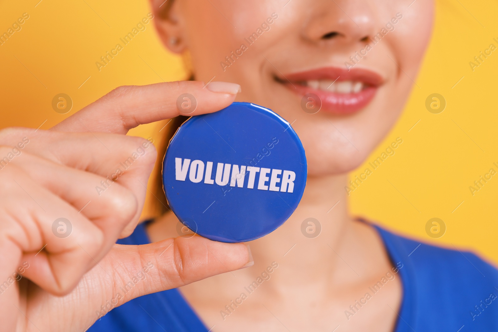 Photo of Woman showing blue button badge with word Volunteer on orange background, closeup