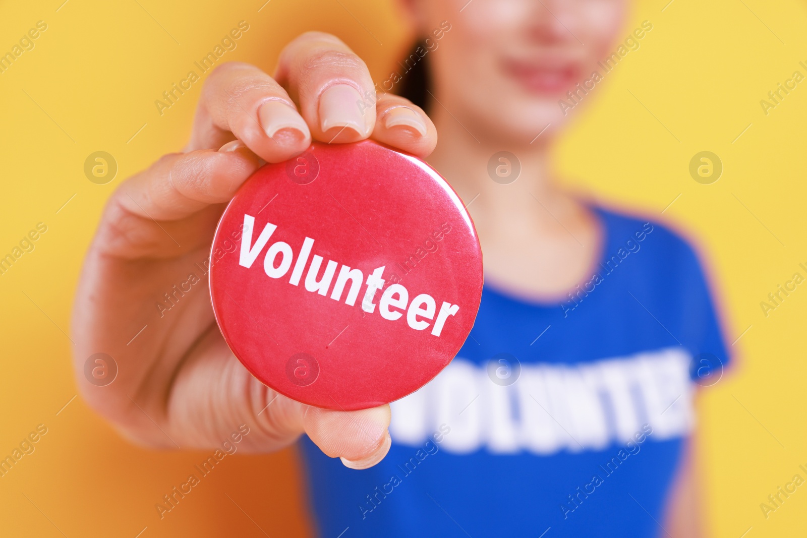 Photo of Woman showing red button badge with word Volunteer on orange background, closeup