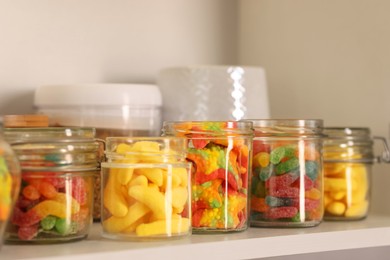 Photo of Tasty gummy candies in jars on shelf, closeup