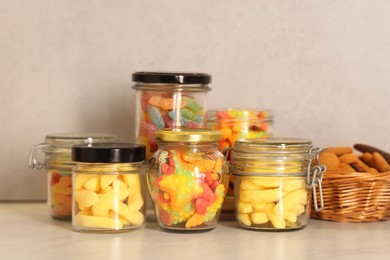 Photo of Tasty gummy candies in glass jars on light table