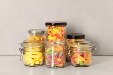 Photo of Tasty gummy candies in glass jars on light table