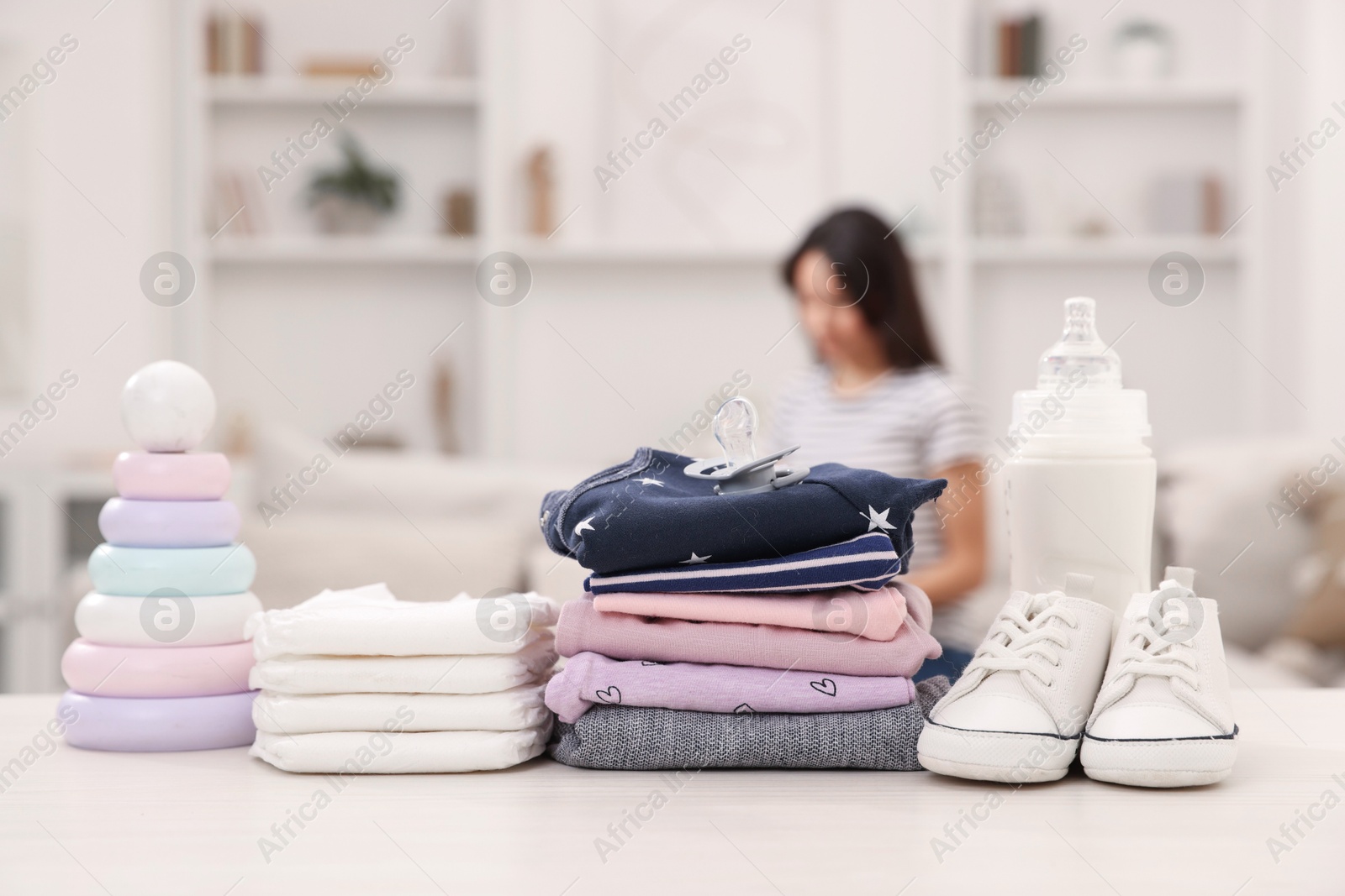 Photo of Baby's stuff on white table and mother packing bag, selective focus