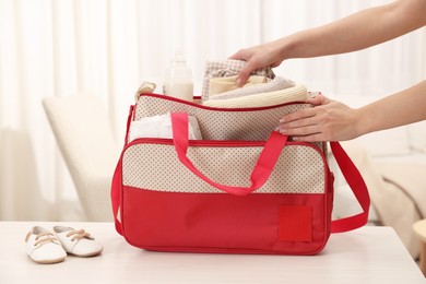 Photo of Mother packing baby's stuff into bag at white table, closeup