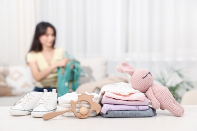 Photo of Baby's stuff on white table and mother packing bag, selective focus