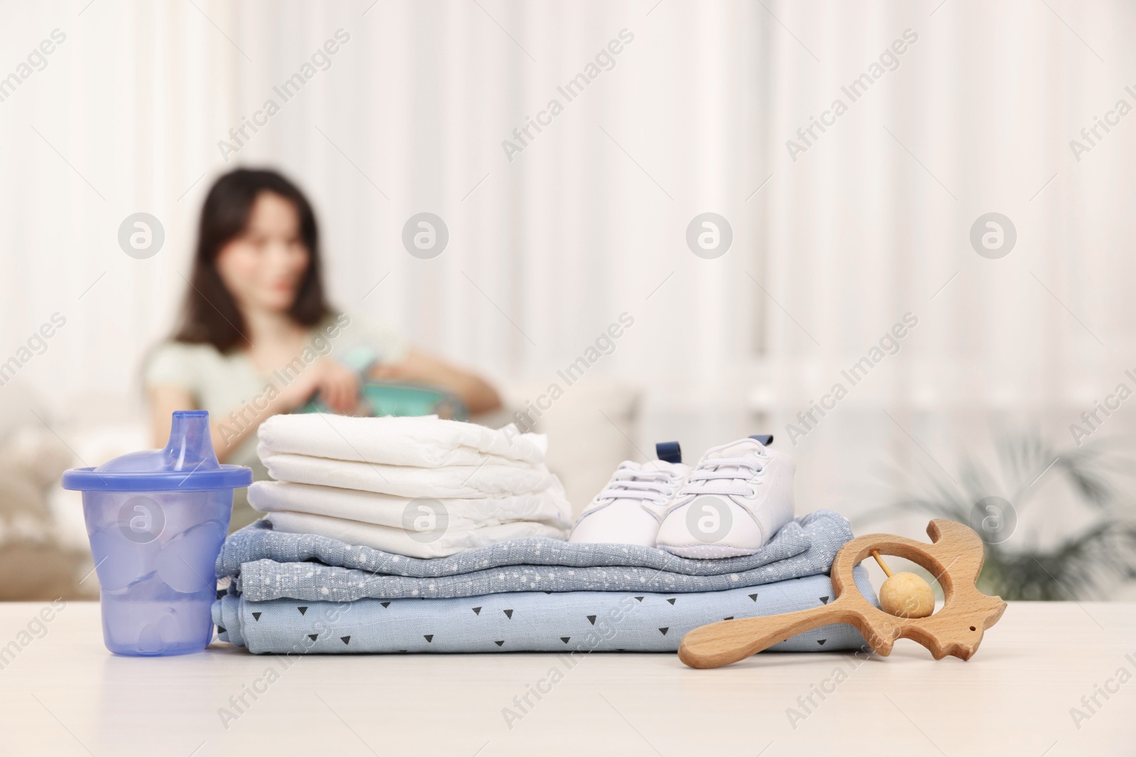 Photo of Baby's stuff on white table and mother packing bag, selective focus