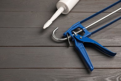 Photo of Glue gun and tube on gray wooden background, closeup. Space for text