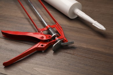 Photo of One glue gun and tube on wooden background, closeup. Construction tool