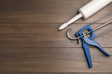 Photo of One glue gun and tube on wooden background, top view with space for text. Construction tool