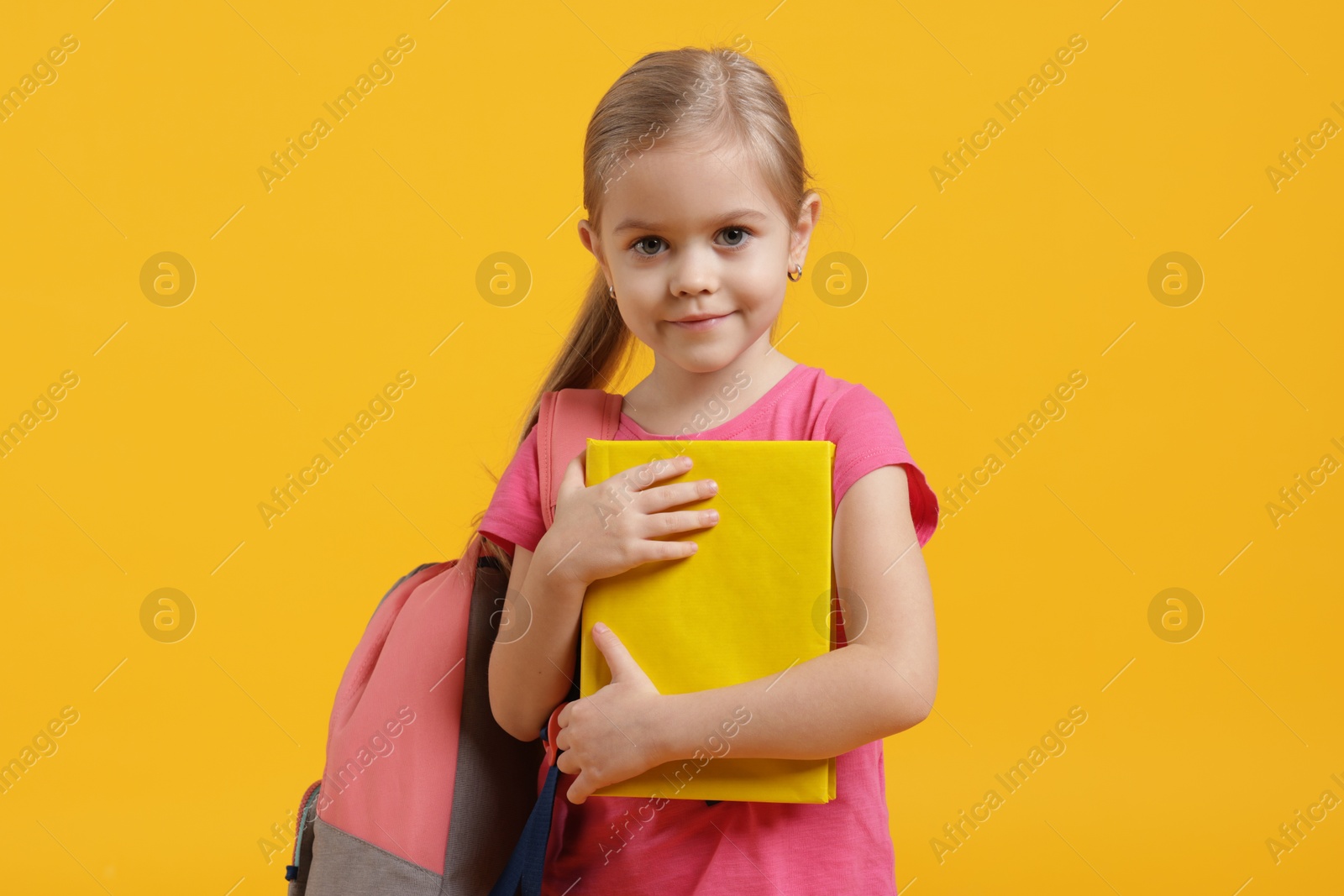 Photo of Cute little schoolgirl with backpack and book on orange background