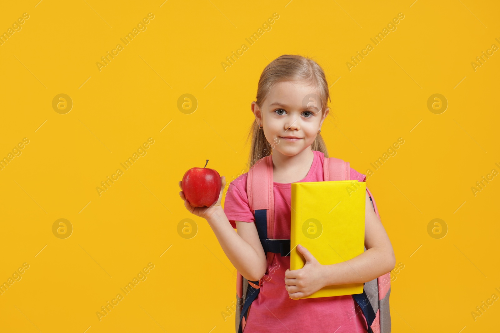 Photo of Cute little girl with book and apple on orange background. Space for text