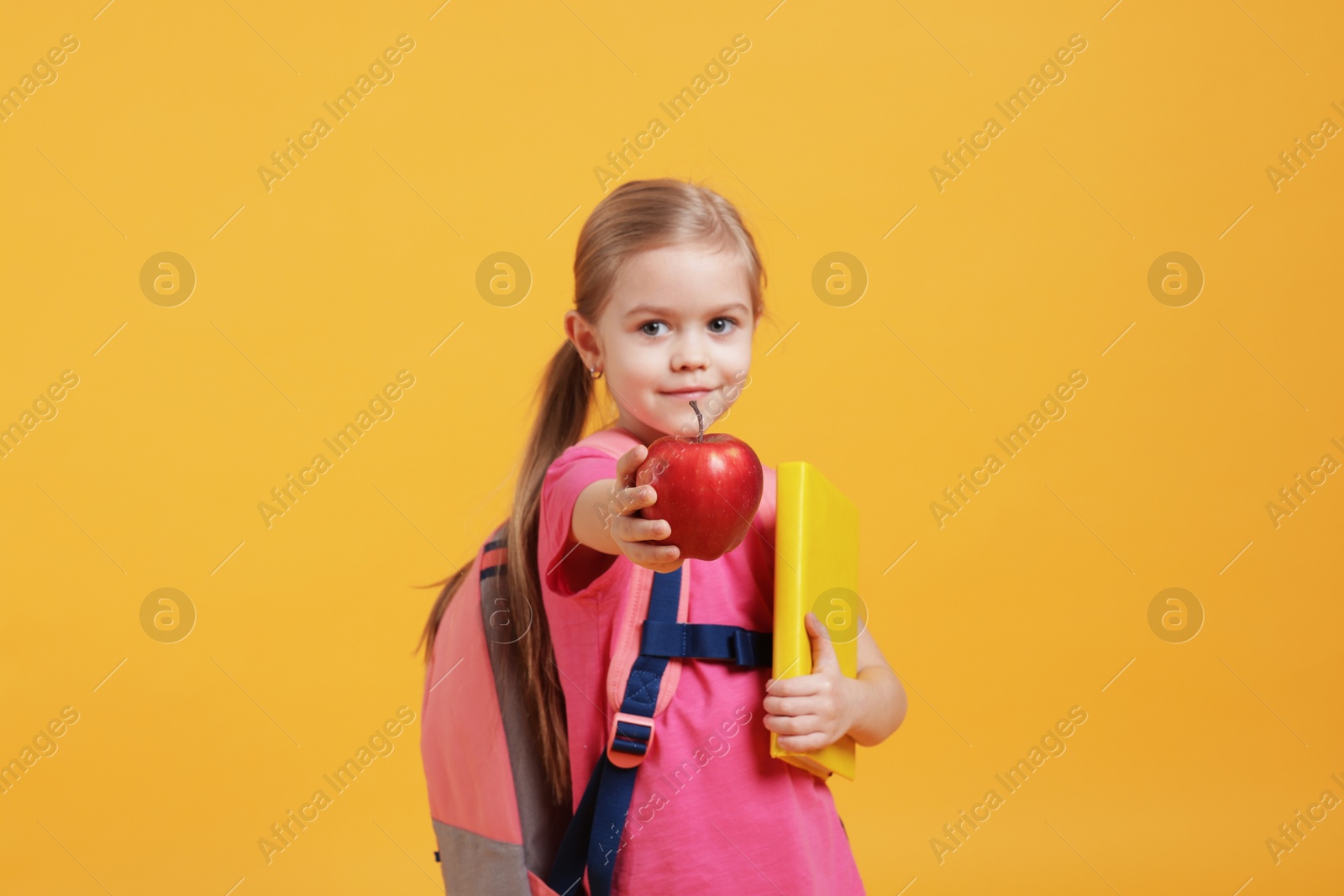 Photo of Cute little girl with book and apple on orange background