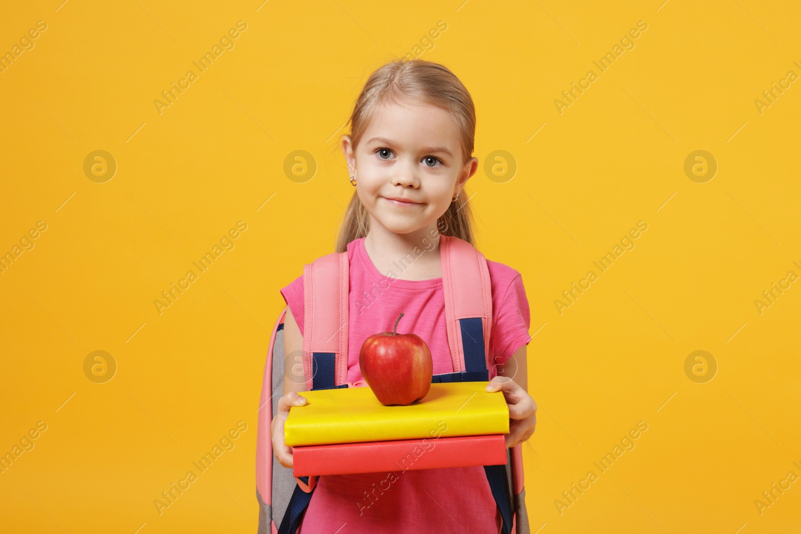 Photo of Cute little girl with books and apple on orange background