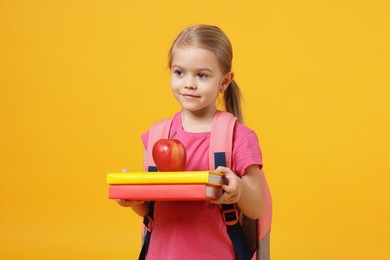 Photo of Cute little girl with books and apple on orange background