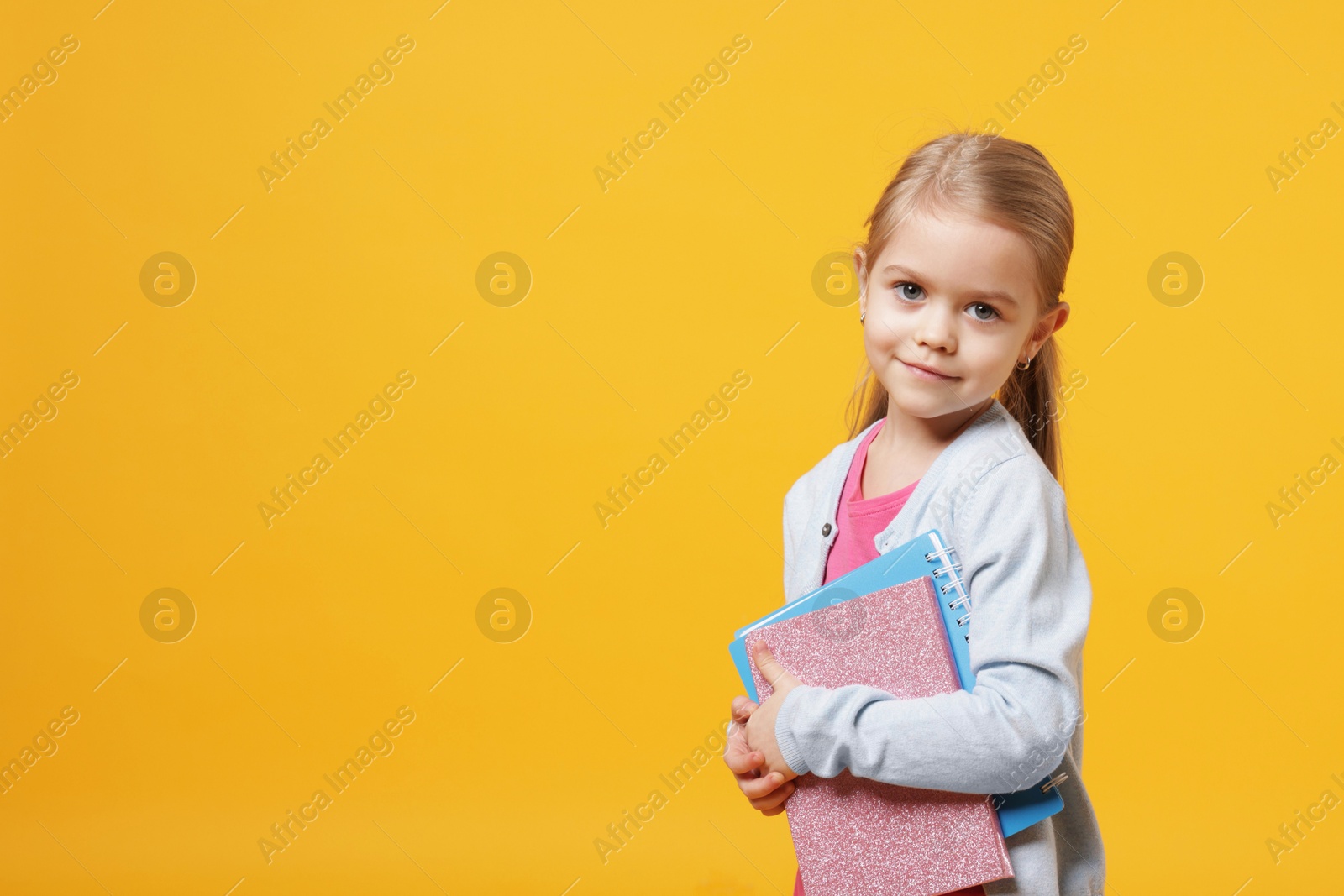 Photo of Cute little schoolgirl with books on orange background. Space for text